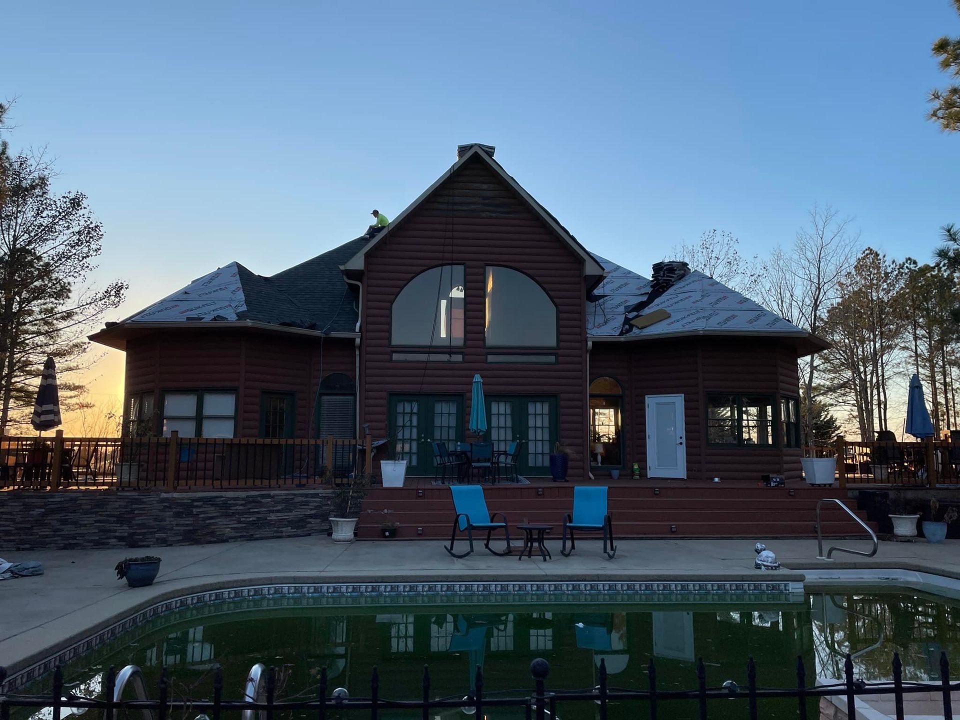 Log cabin home with a pool and deck at dusk. The sky is blue and the sun is setting.