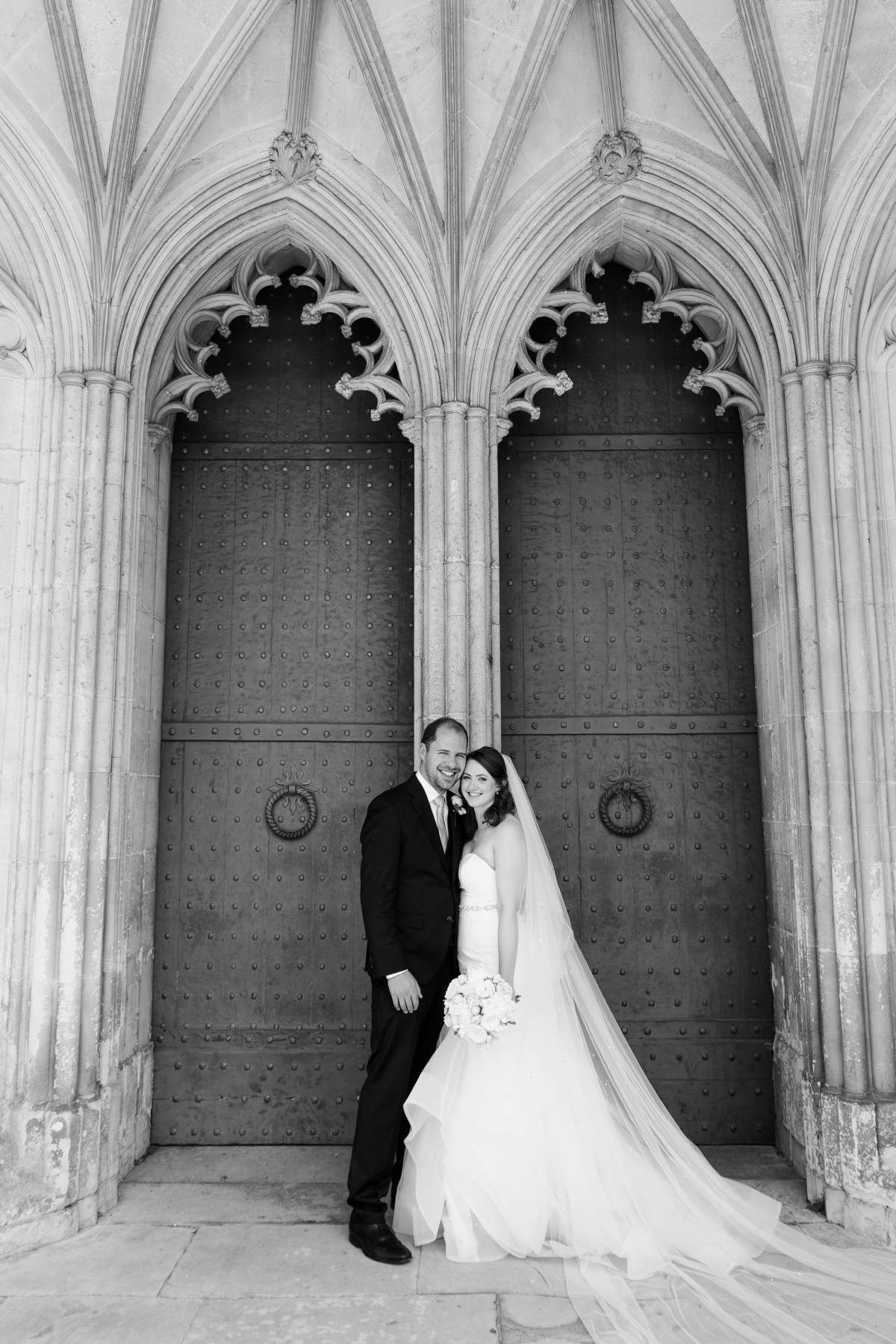 A black and white photo of a bride and groom posing for a picture in front of a door.