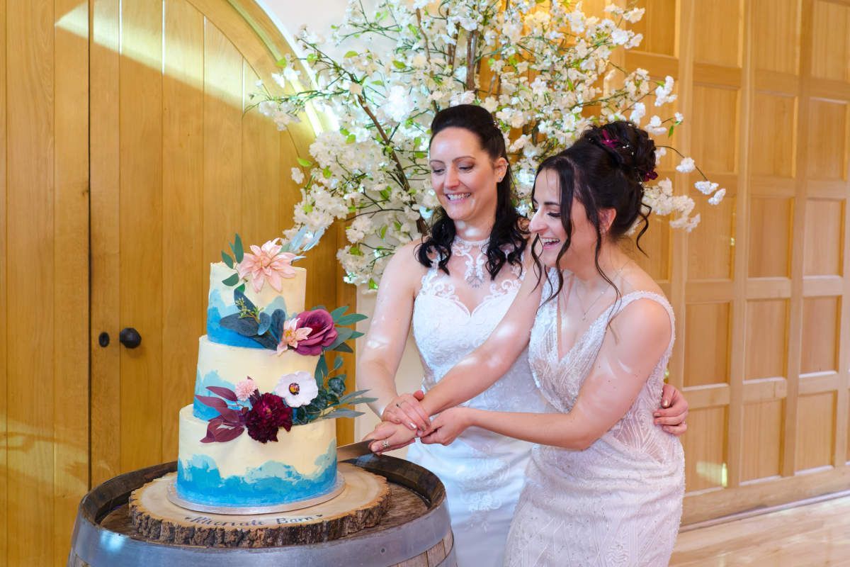 Two women are kissing in front of a wedding cake.