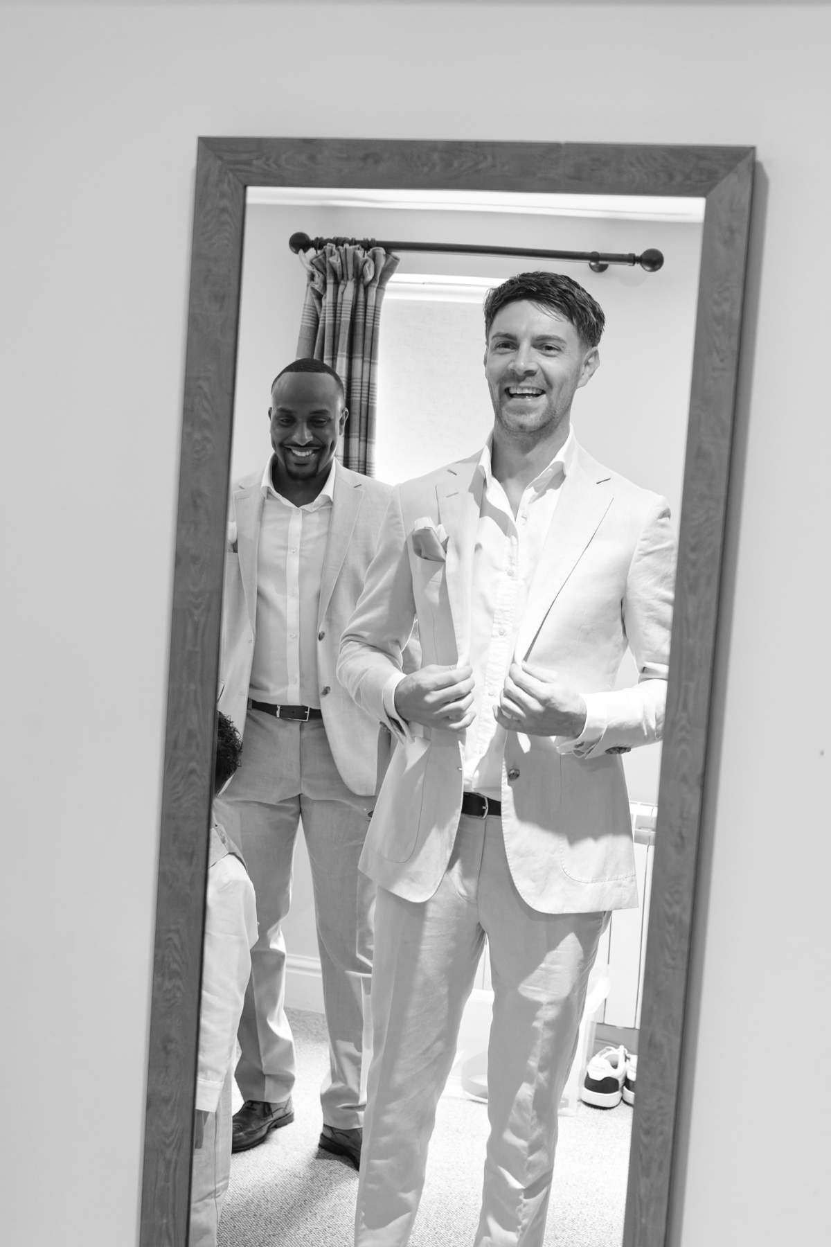 Two men in suits are standing in front of a mirror.