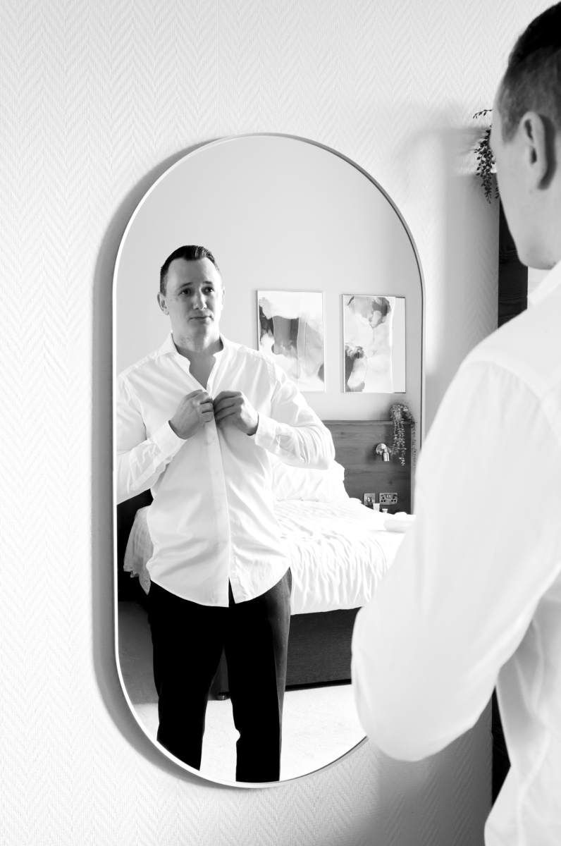 A man in a white shirt is looking at himself in a mirror.