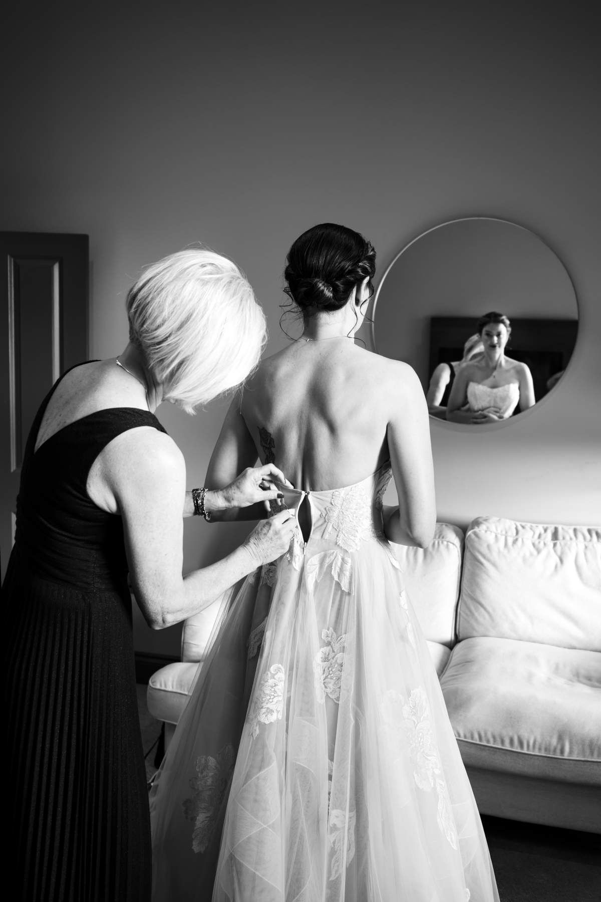 A woman is helping a bride get ready for her wedding in a black and white photo.