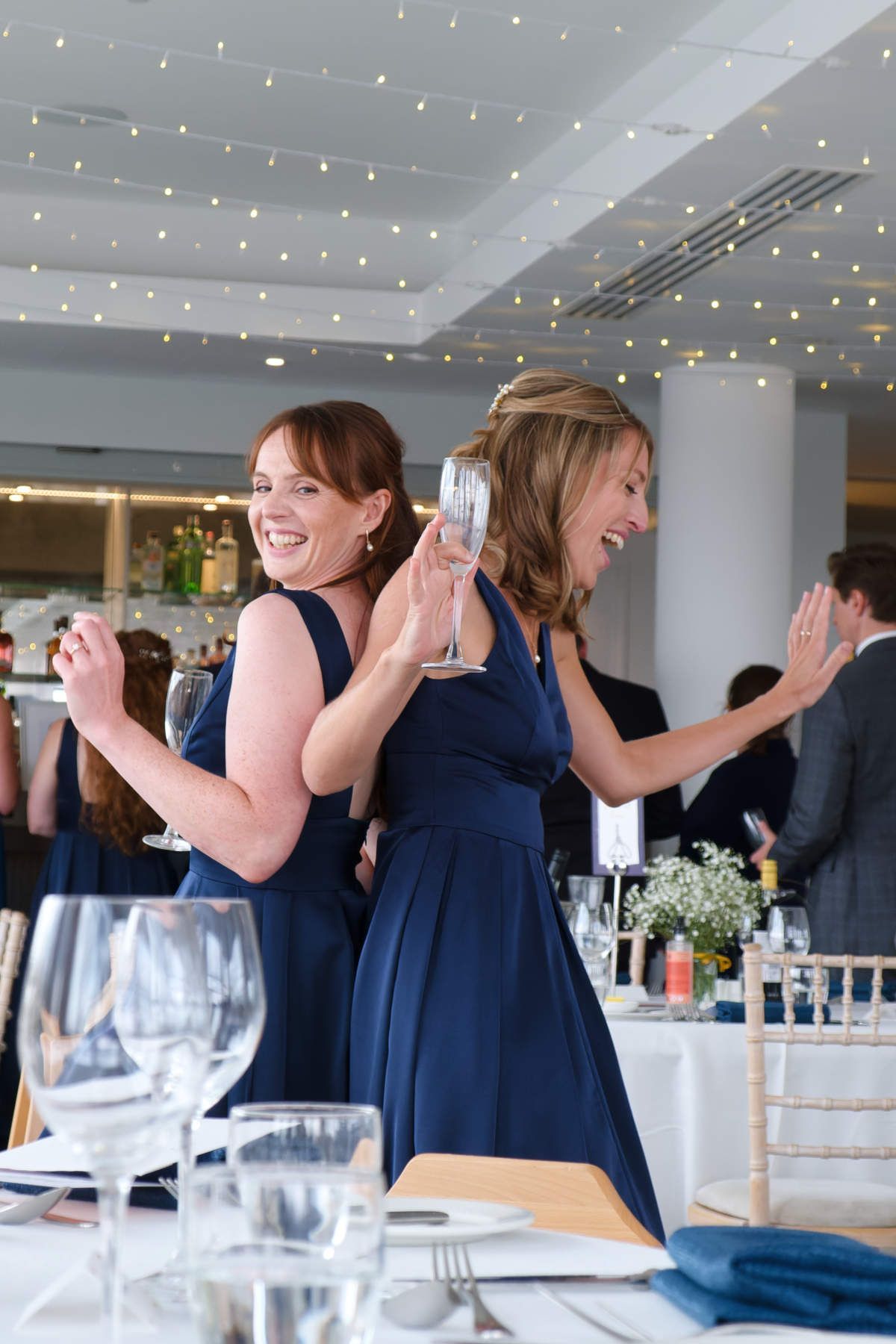 Two women in blue dresses are standing next to each other holding champagne glasses.