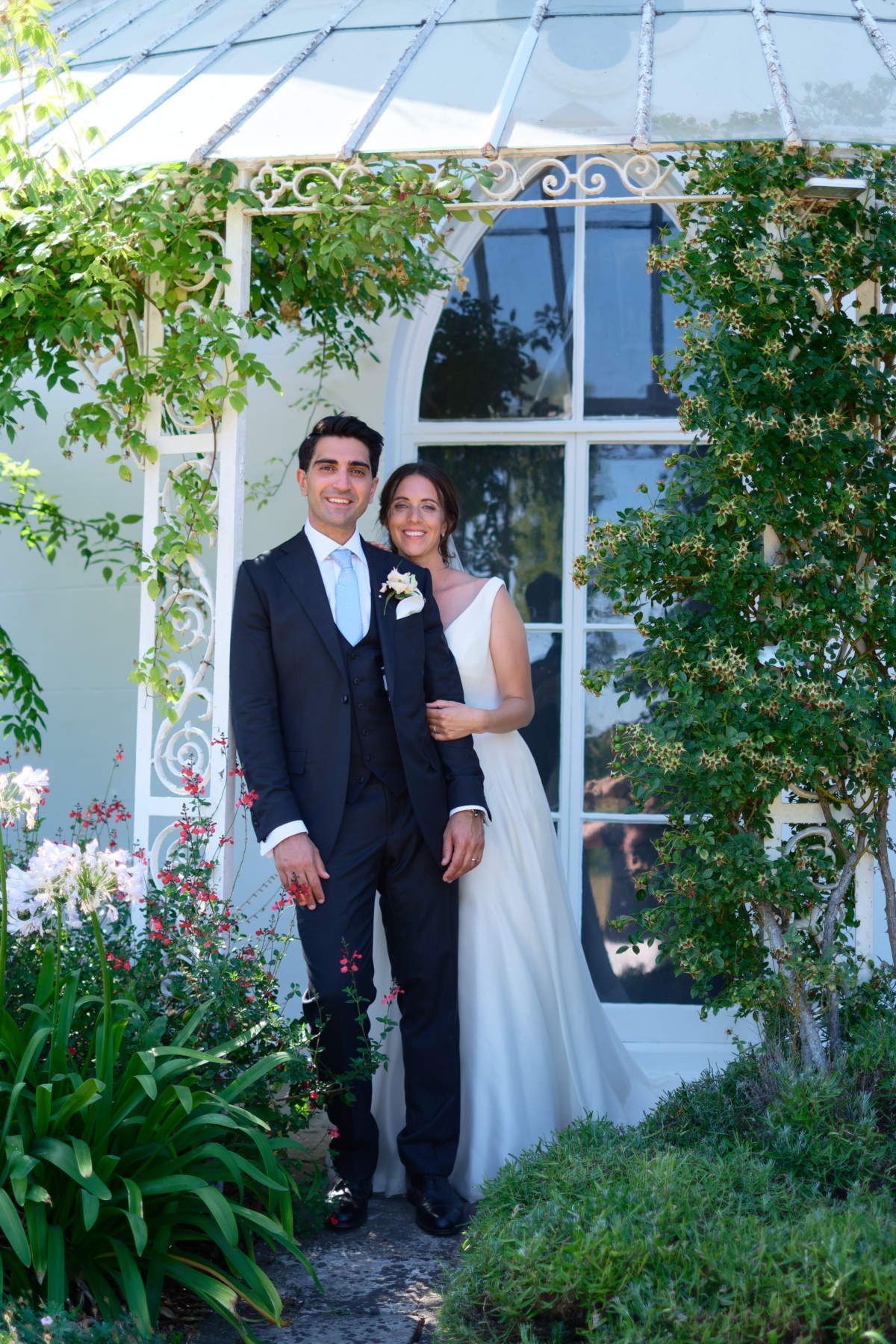 A bride and groom are posing for a picture in front of a greenhouse.
