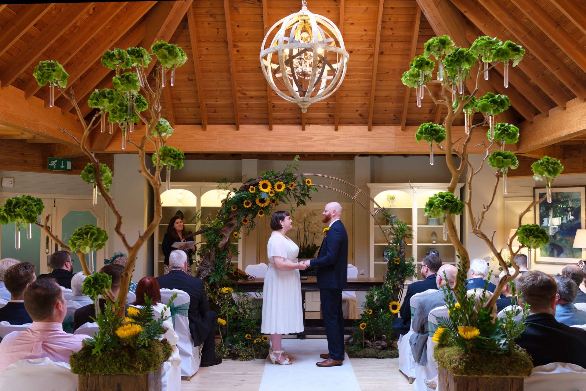 A bride and groom are holding hands during their wedding ceremony in front of a crowd.