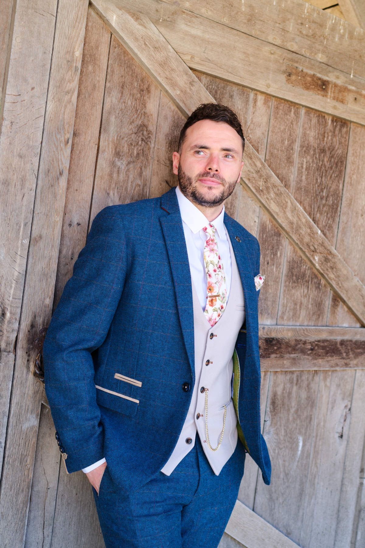 A man in a blue suit and tie is standing in front of a wooden door.