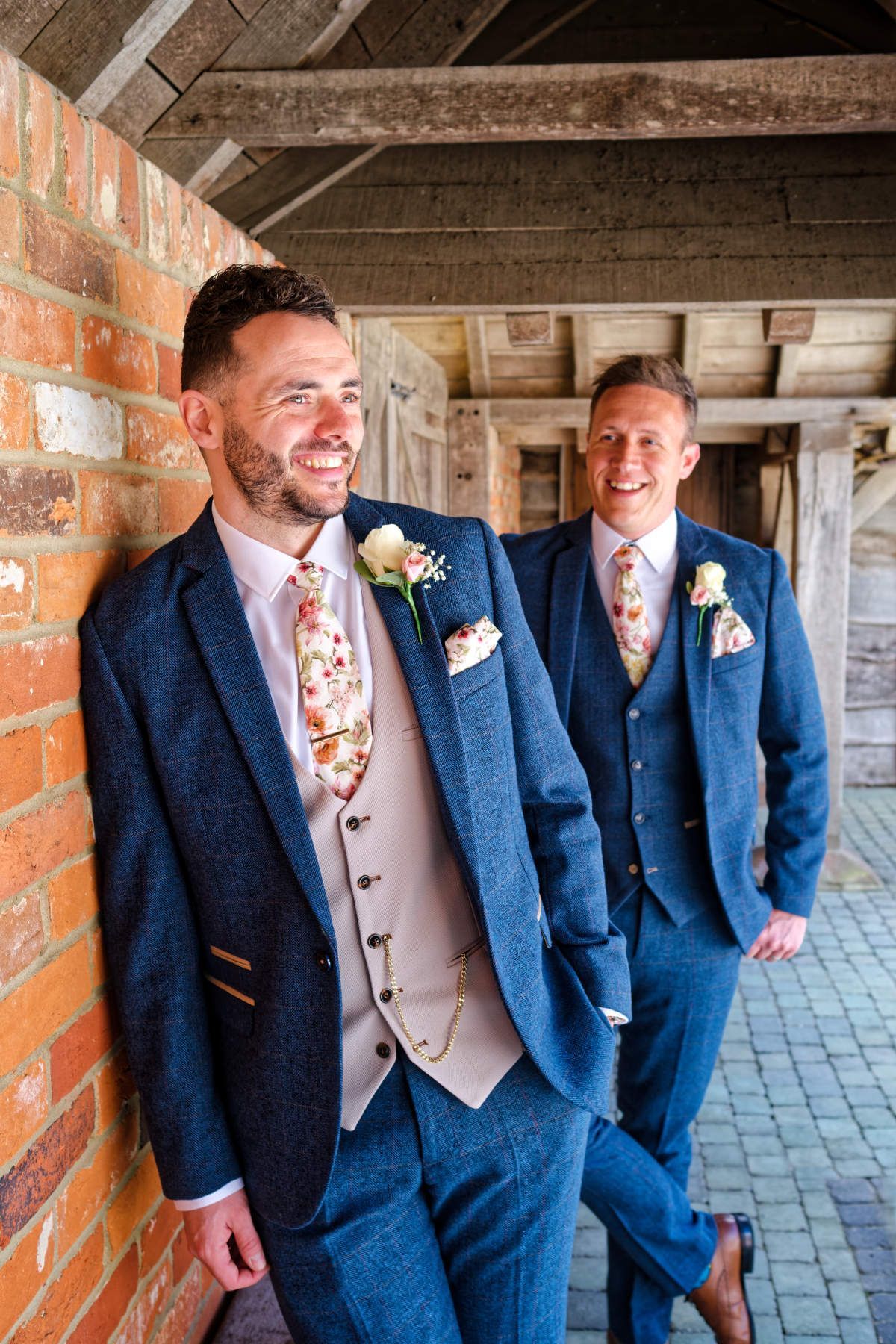 Two men in suits and ties are leaning against a brick wall.