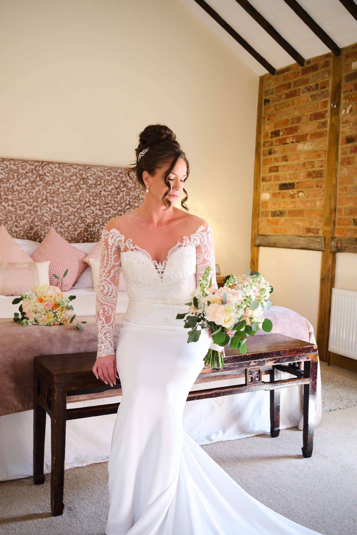 A woman in a wedding dress is holding a bouquet of flowers in a bedroom.