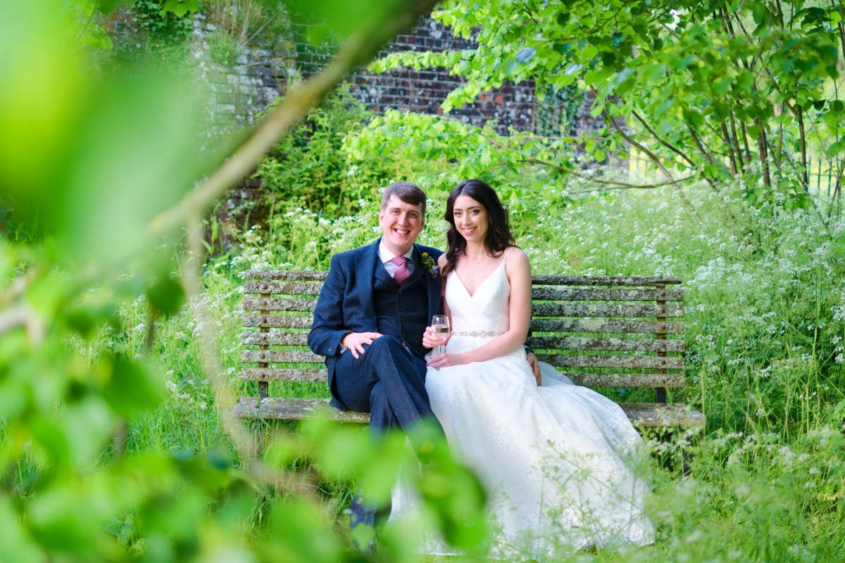 A bride and groom are sitting on a bench in a park.
