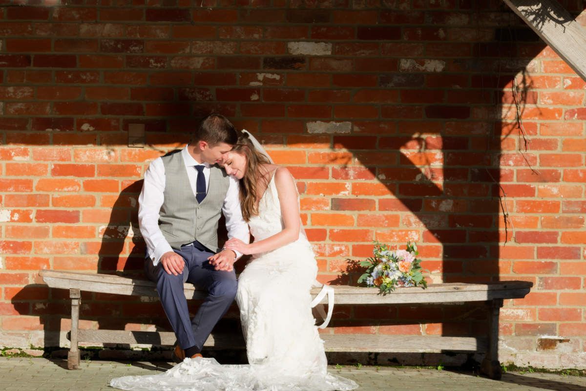 A bride and groom are sitting on a bench in front of a brick wall.