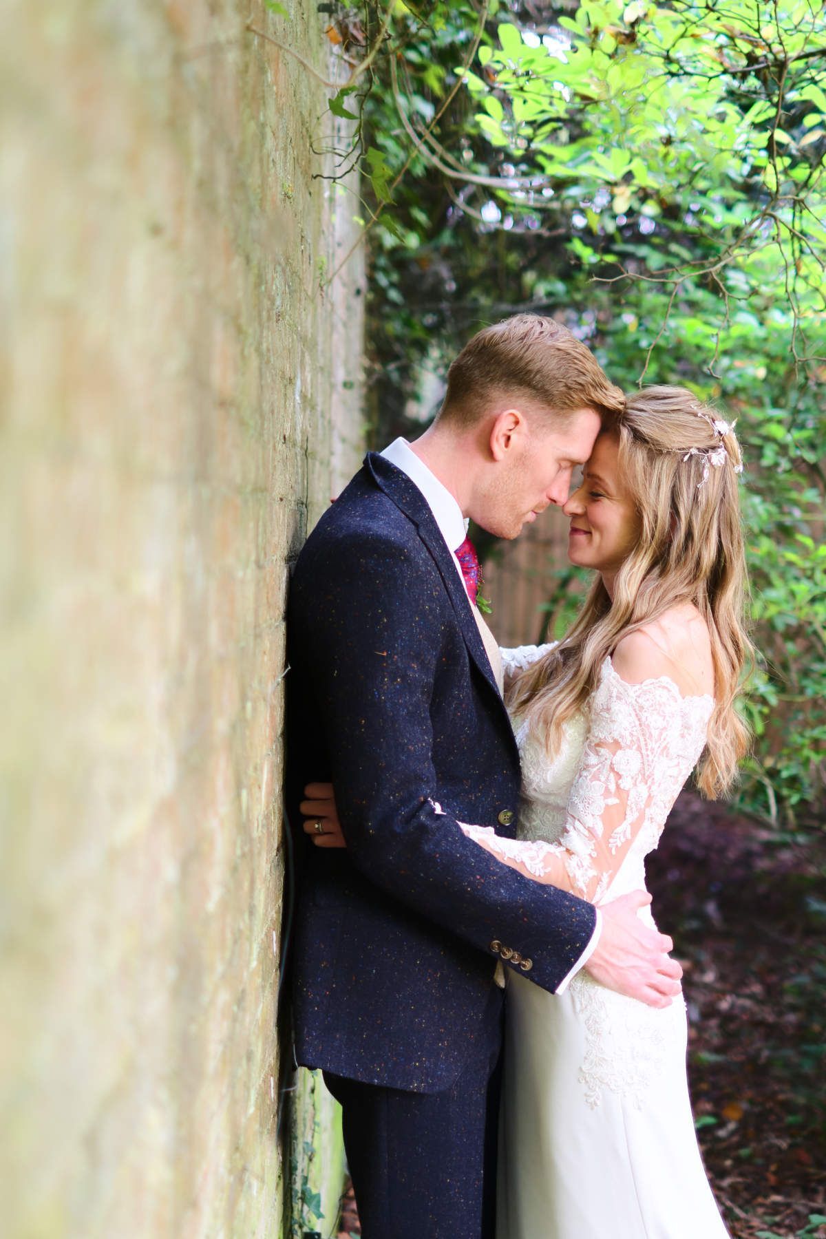 A bride and groom are leaning against a wall and kissing.