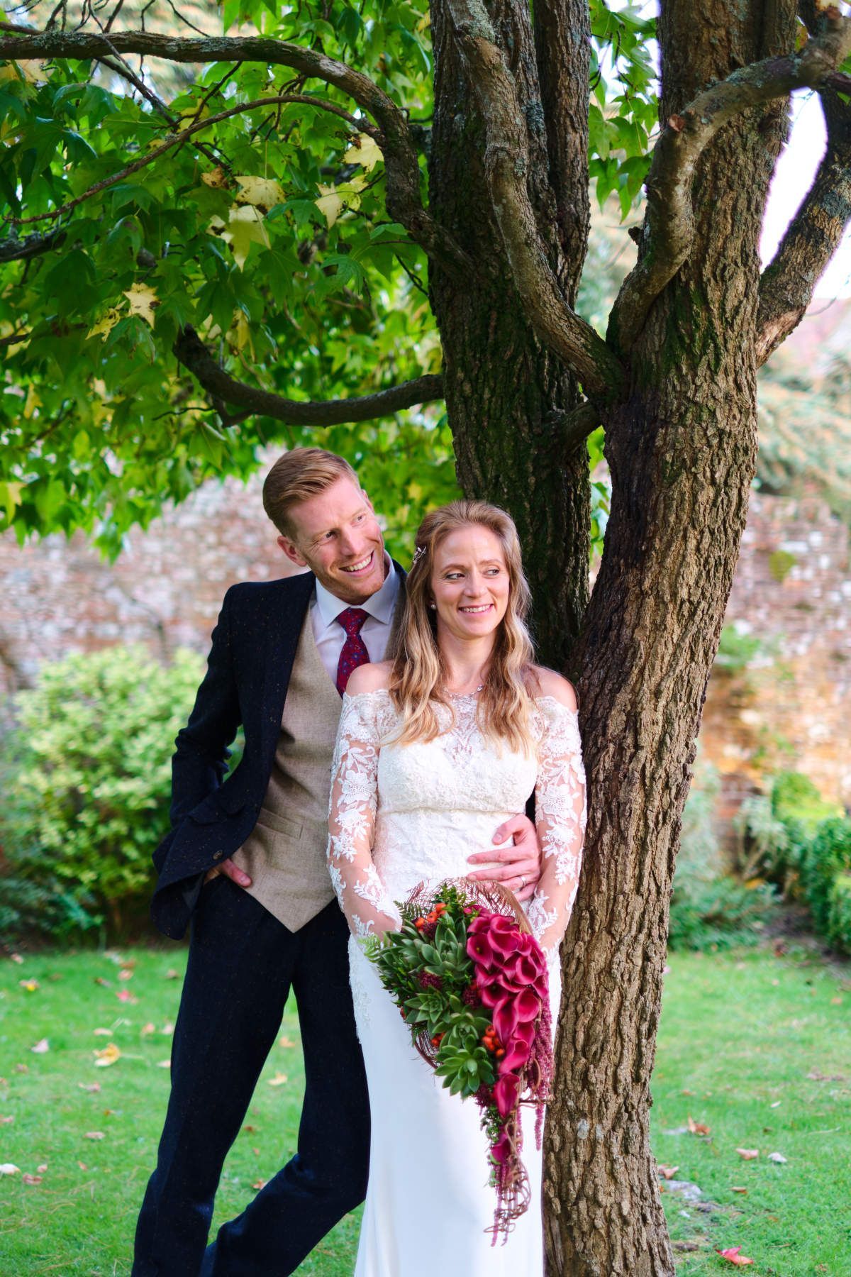 A bride and groom are posing for a picture next to a tree.
