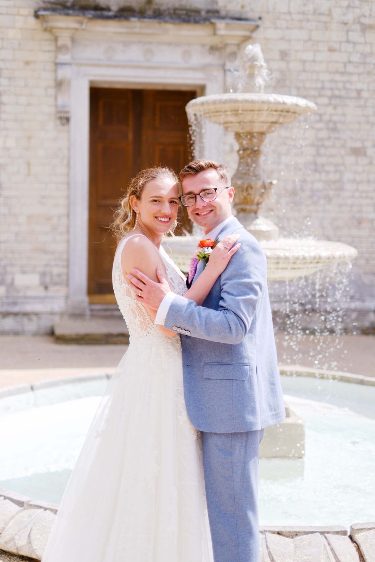 A bride and groom are posing for a picture in front of a fountain.