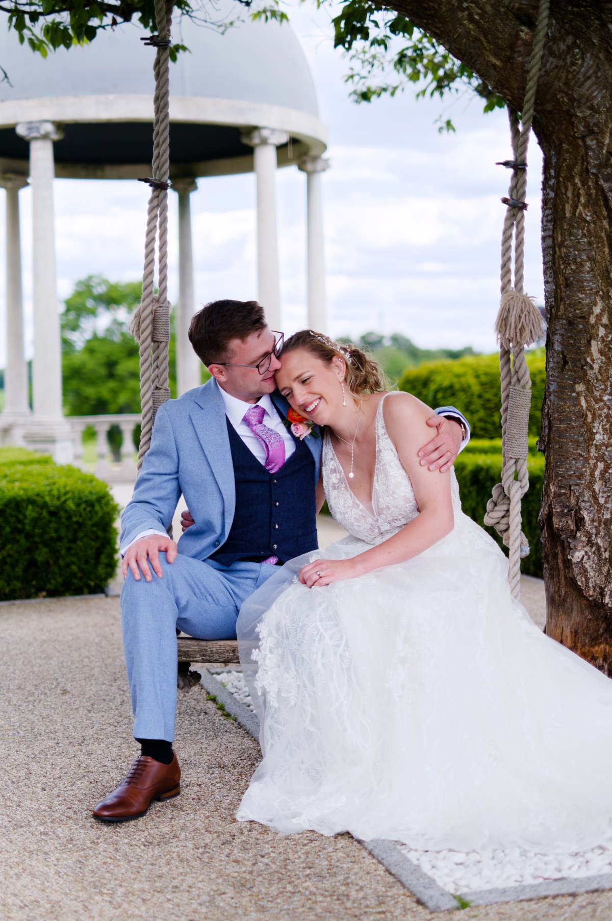 A bride and groom are sitting on a swing under a gazebo.