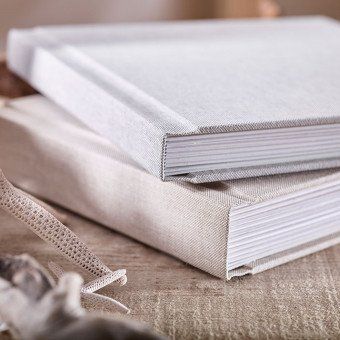 two white wedding albums are stacked on top of each other on a wooden table .