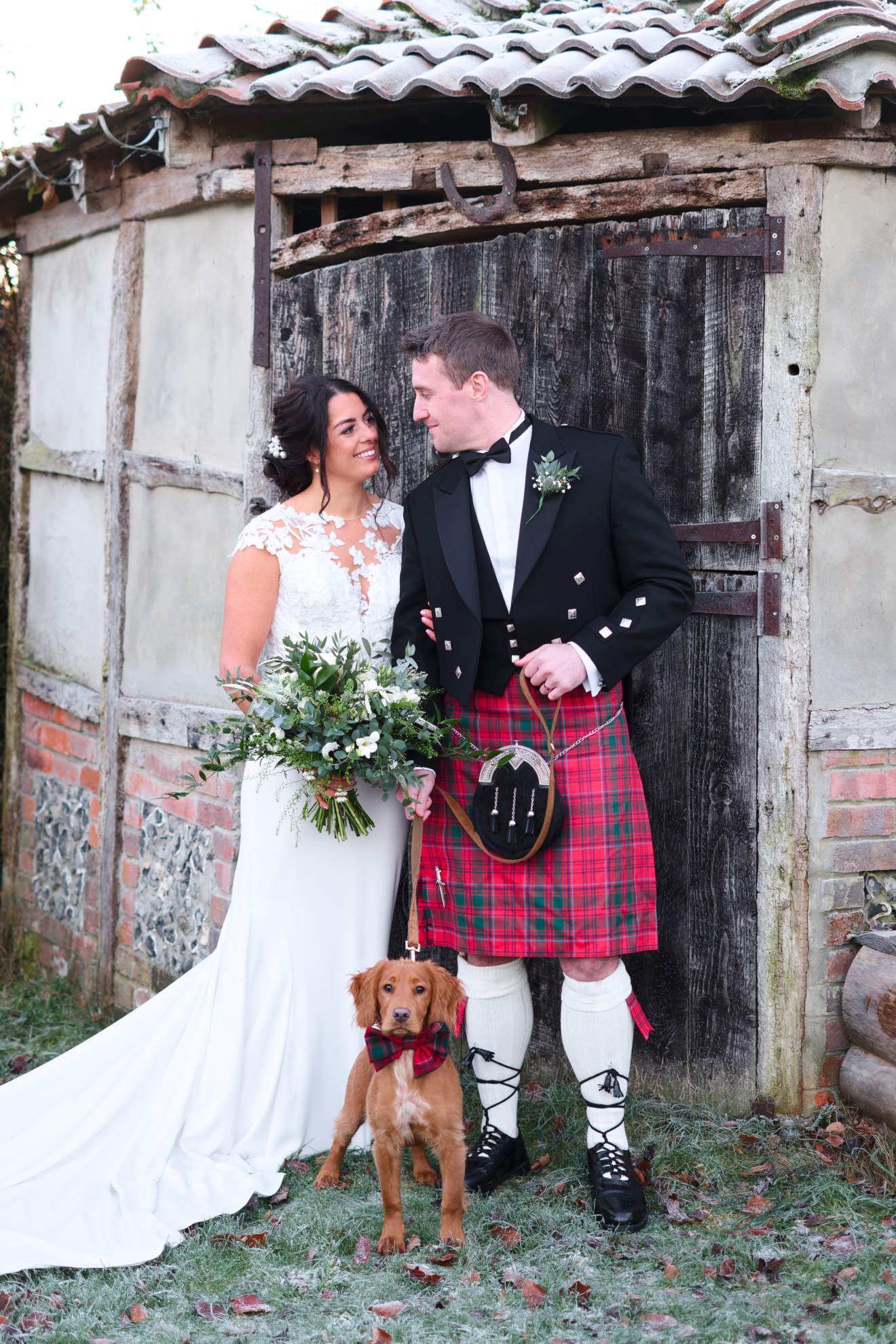A bride and groom are posing for a picture with their dog.