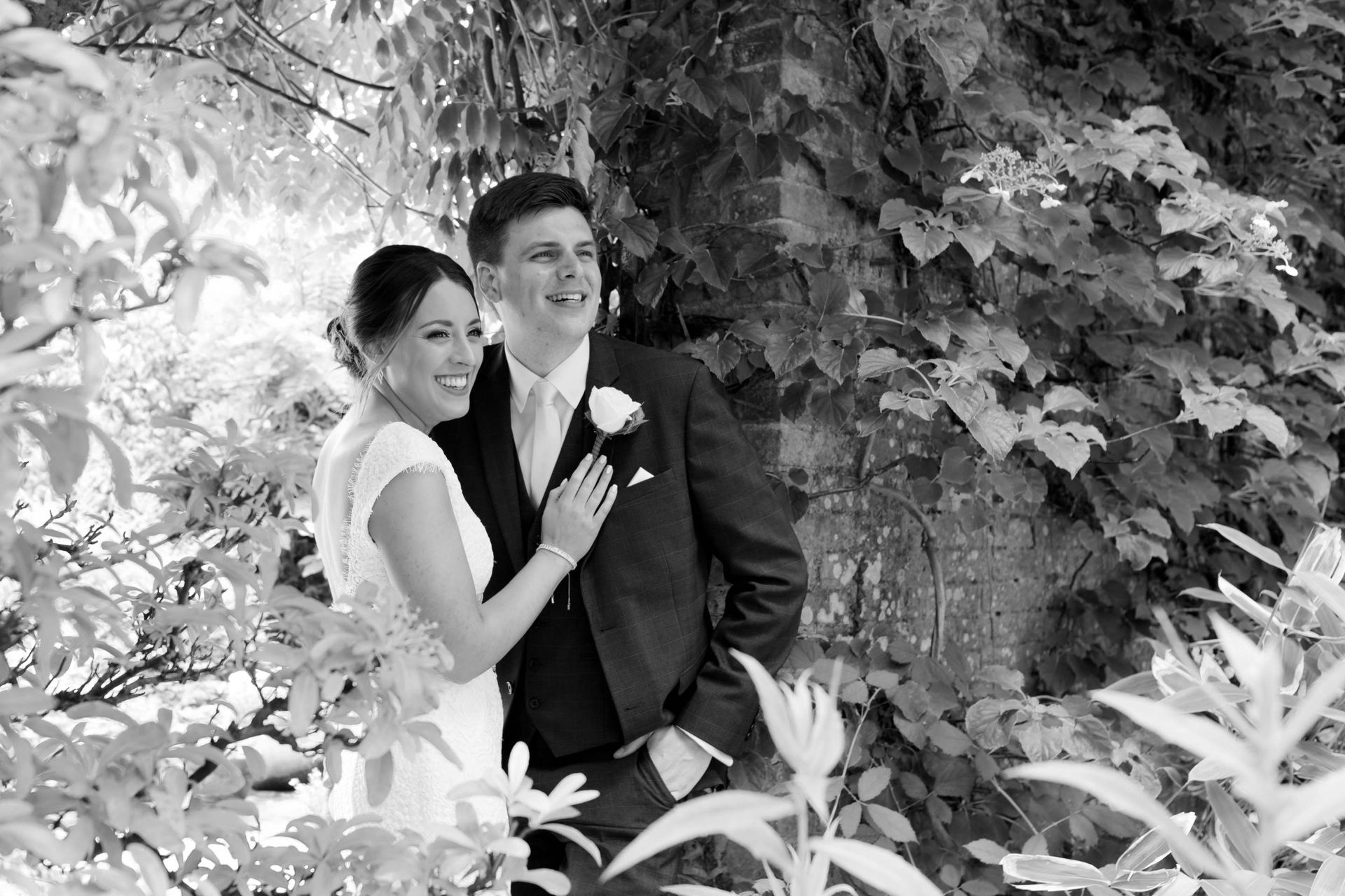 A black and white photo of a bride and groom standing next to a tree.