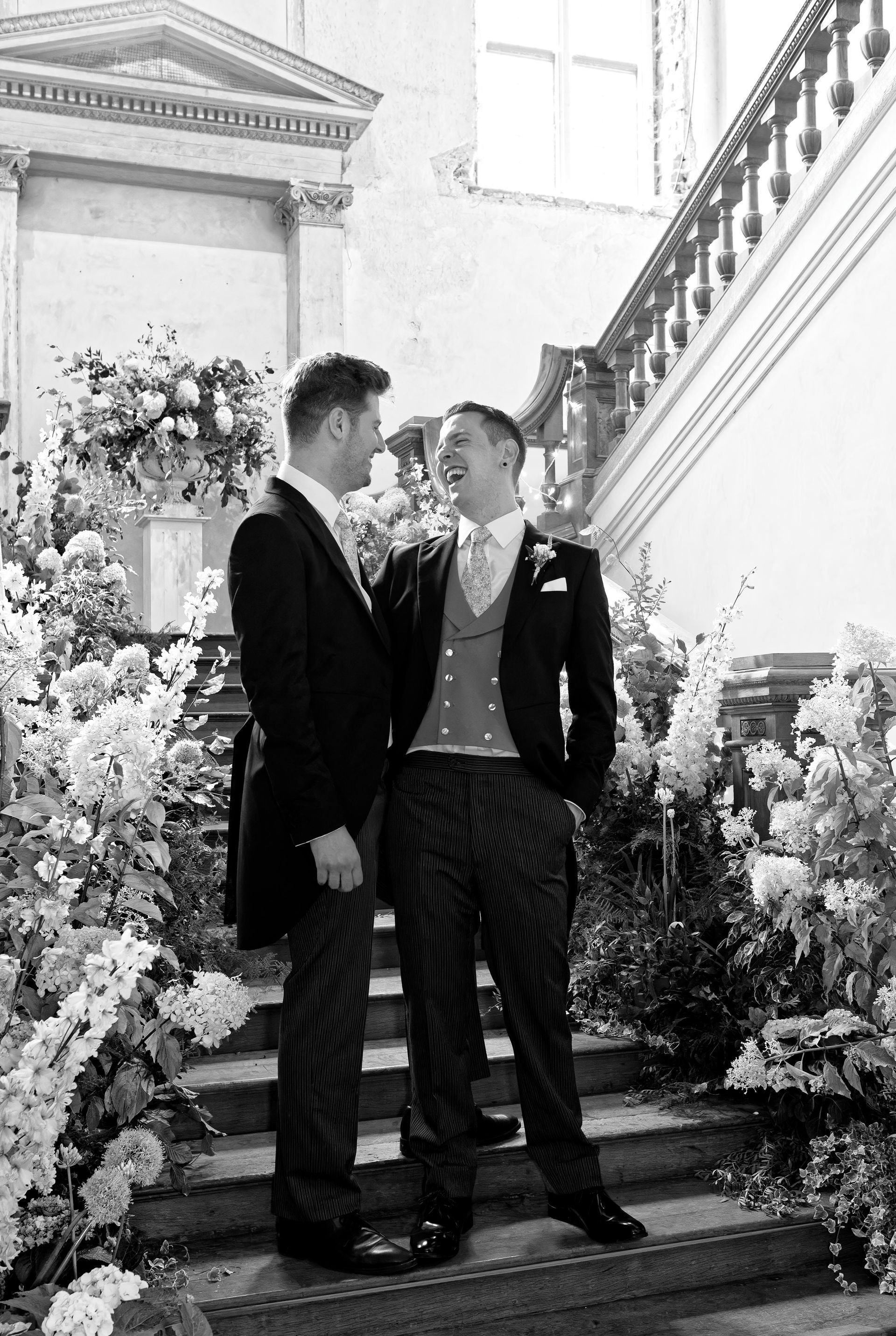 gay wedding photography of two men in suits are standing next to each other on a set of stairs .