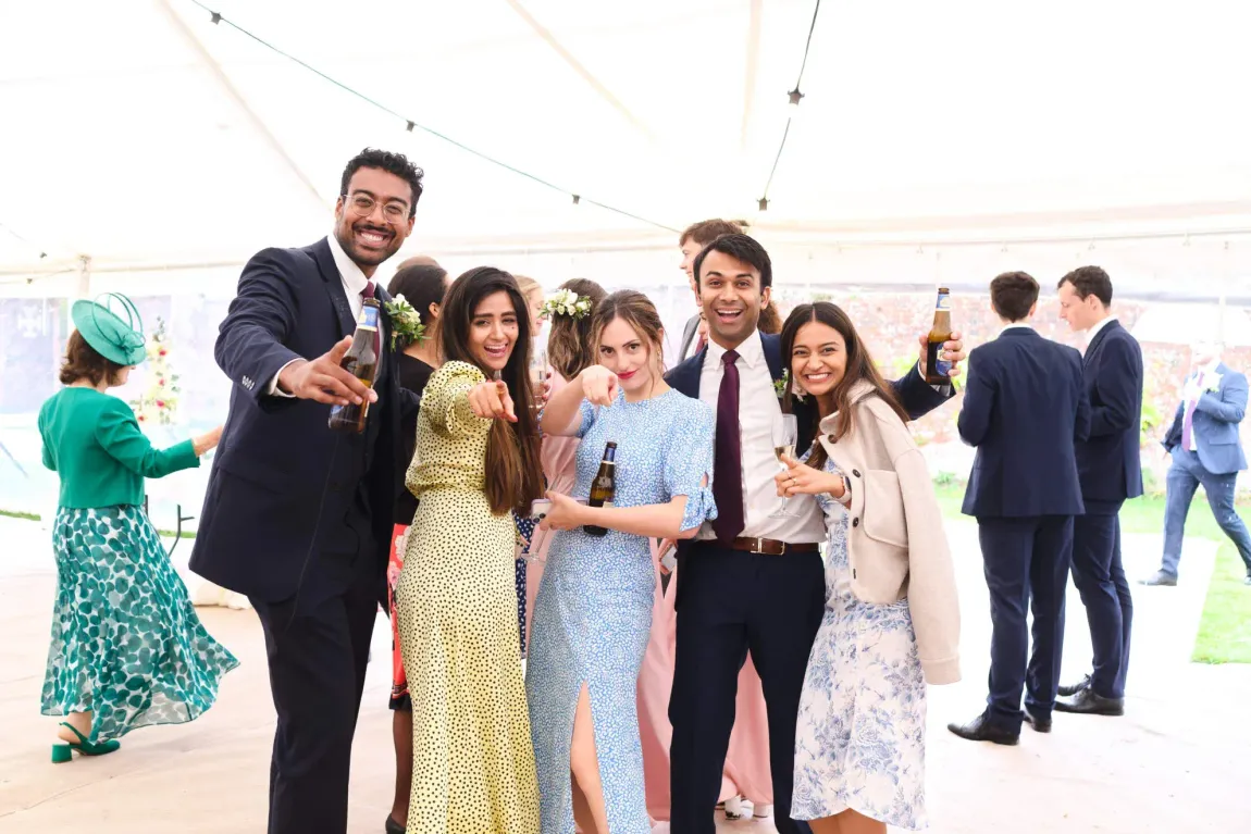 A group of wedding guests are posing for a photo at a wedding reception.