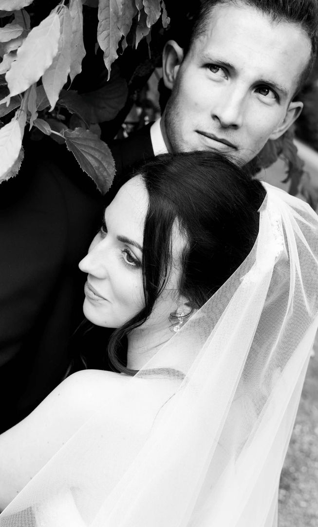 Bride and groom posing together outdoors, bride in veil, groom looking on. Black and white photograph.