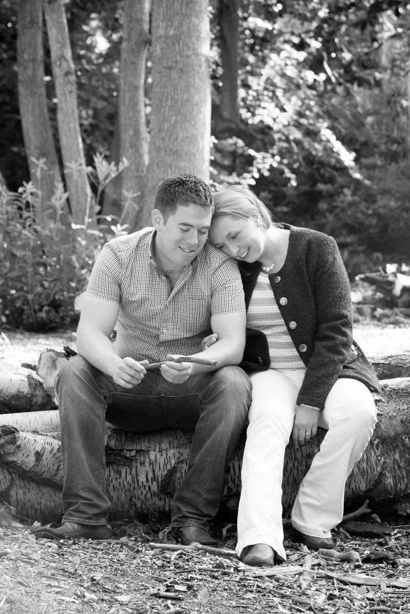 A man and a woman are sitting on a log in the woods.