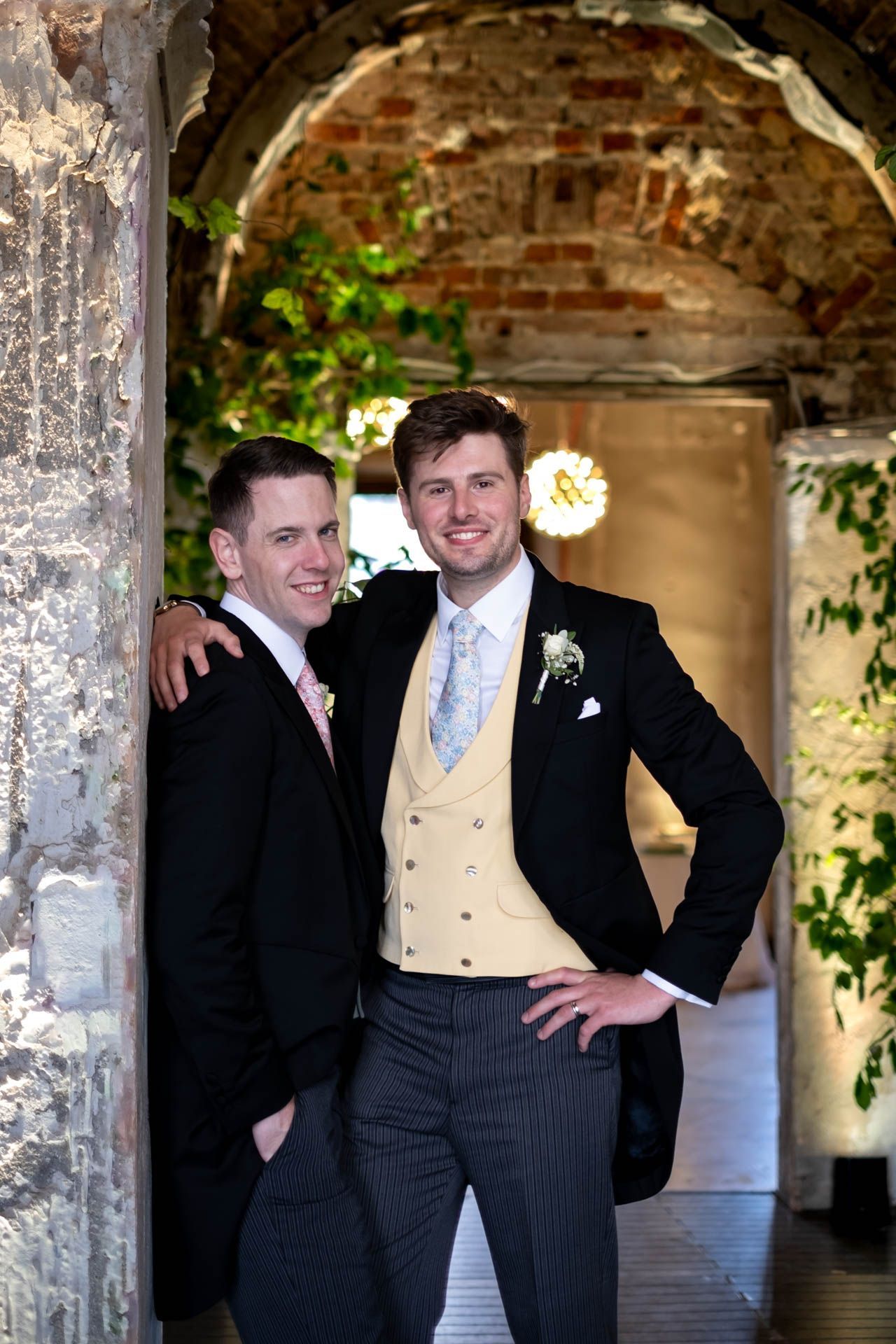 Two men in suits are posing for a picture in front of a brick wall.