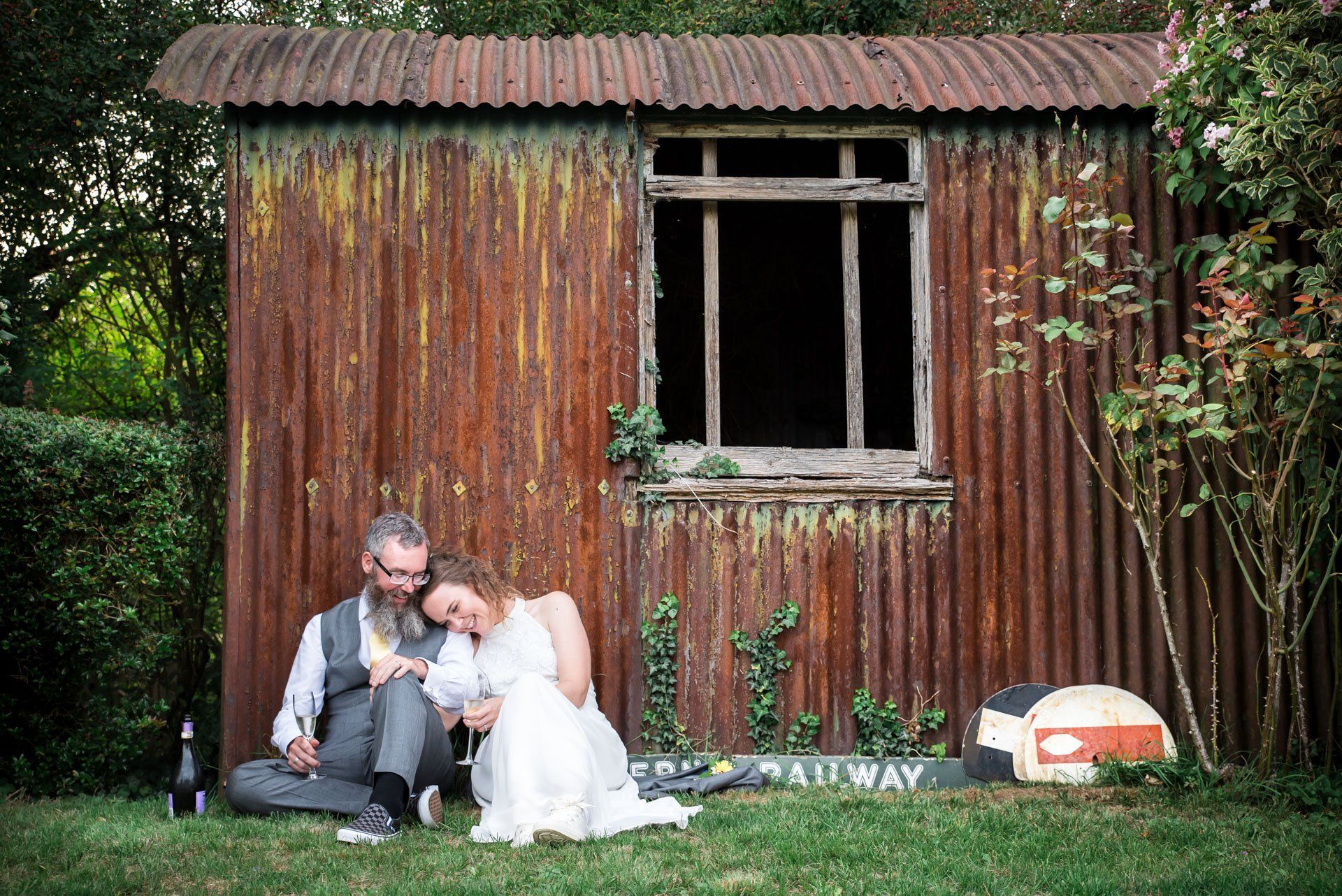 A bride and groom are sitting in front of a rusty shed.