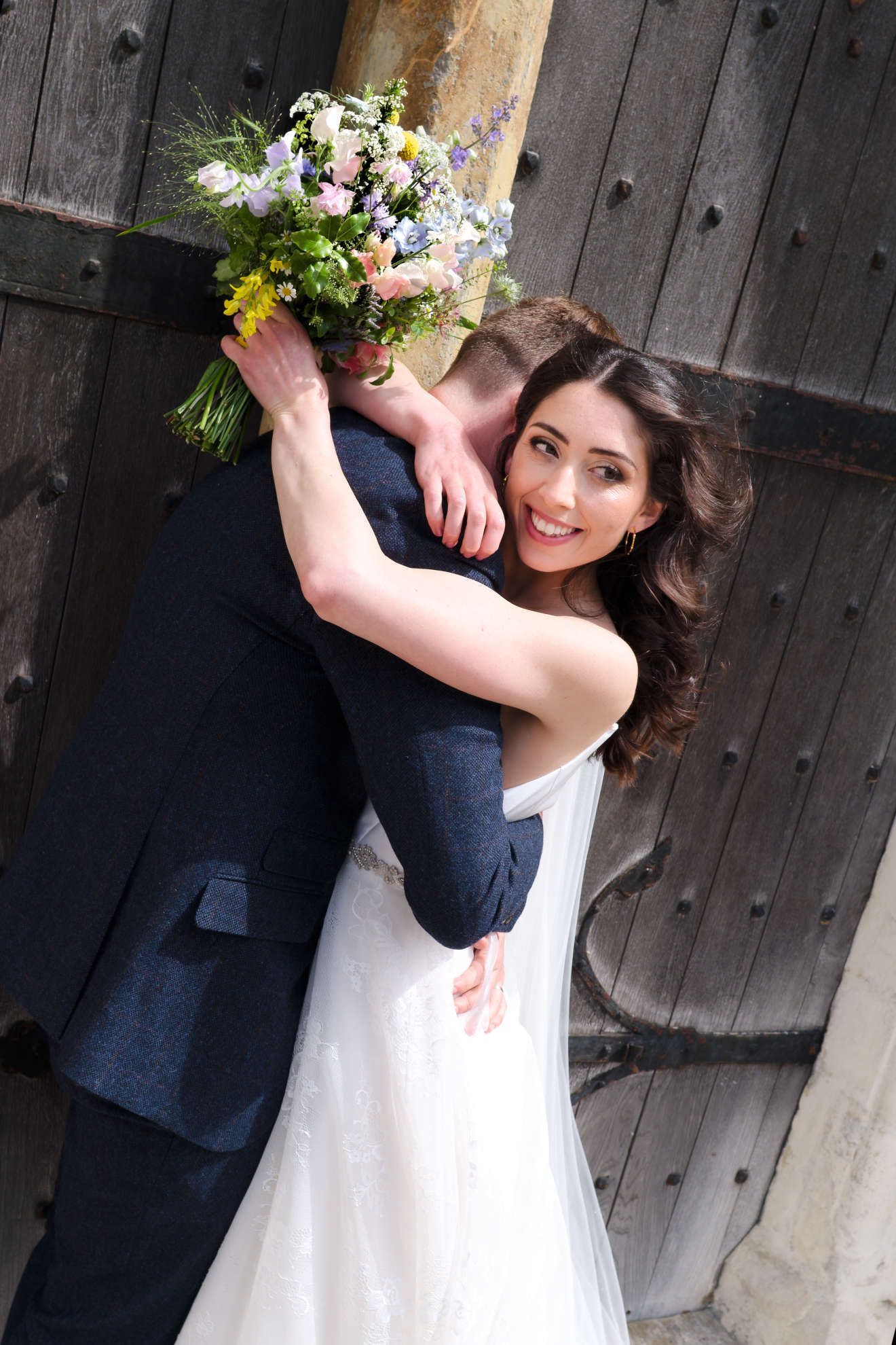 A bride and groom are hugging each other while the bride is holding a bouquet of flowers.