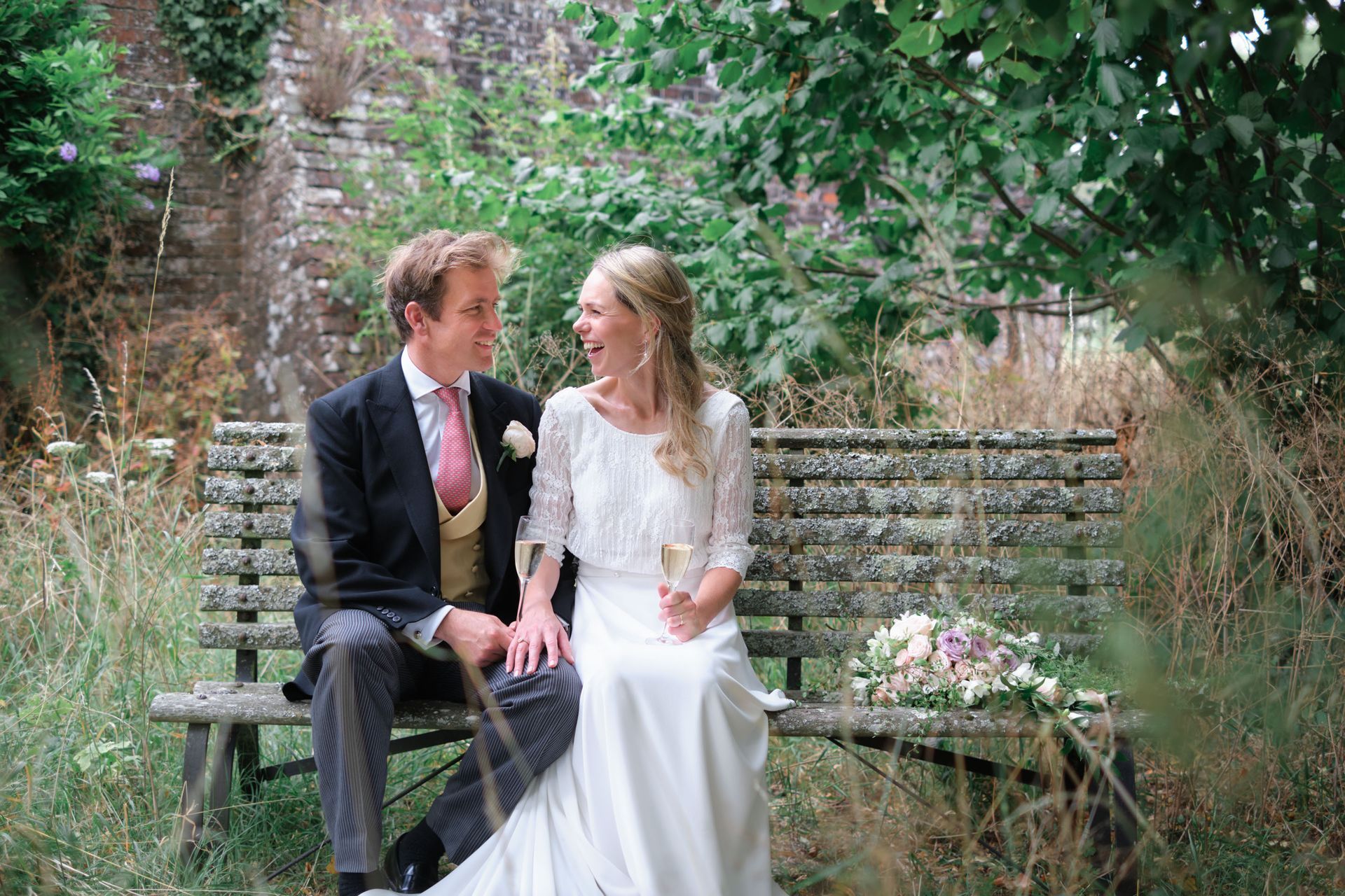 A bride and groom are sitting on a wooden bench.