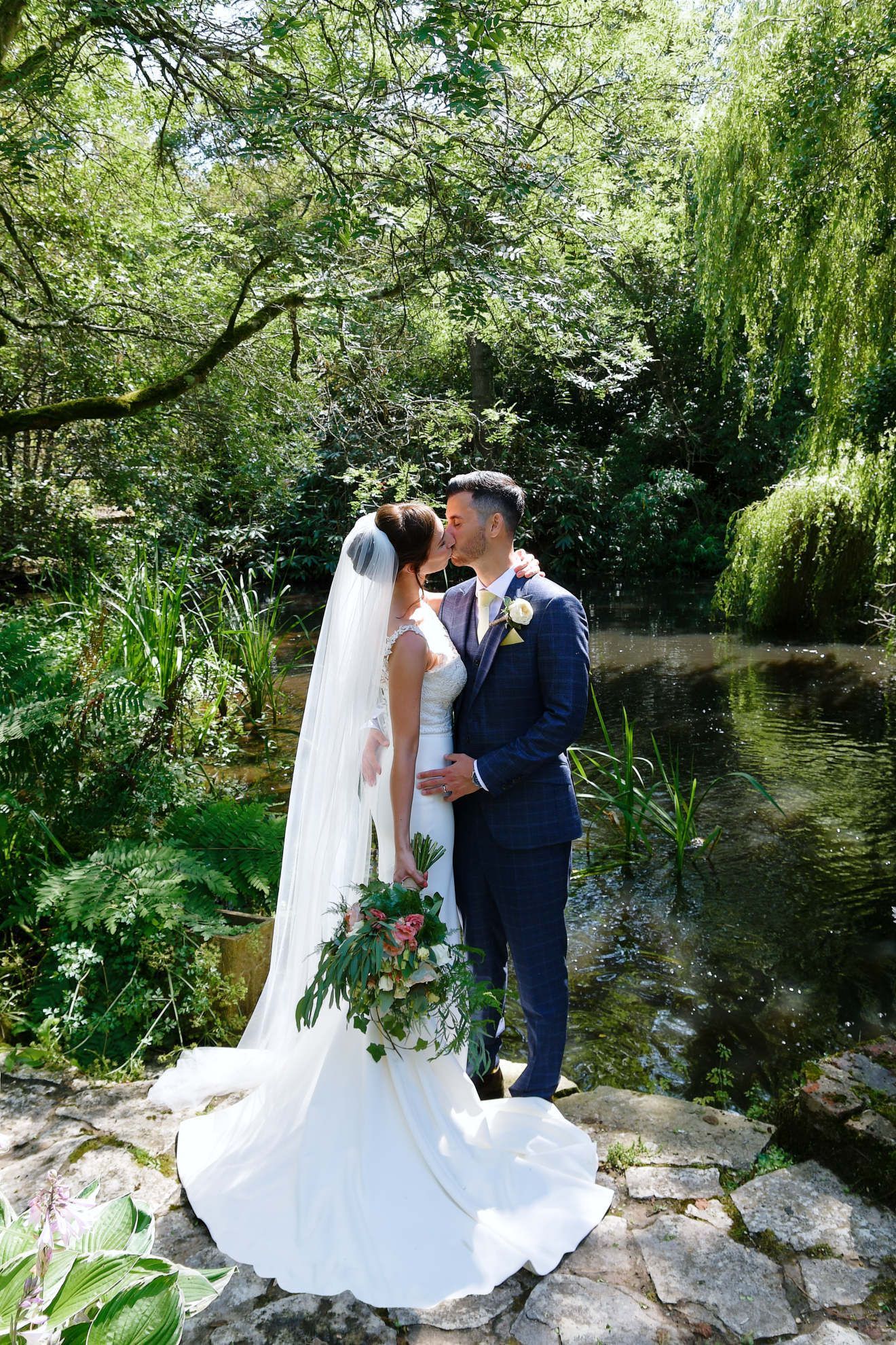 A bride and groom are kissing in front of a pond.