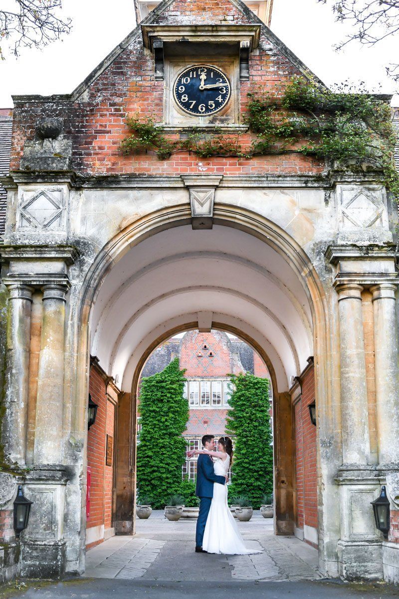 A bride and groom are kissing under an archway in front of a clock tower.