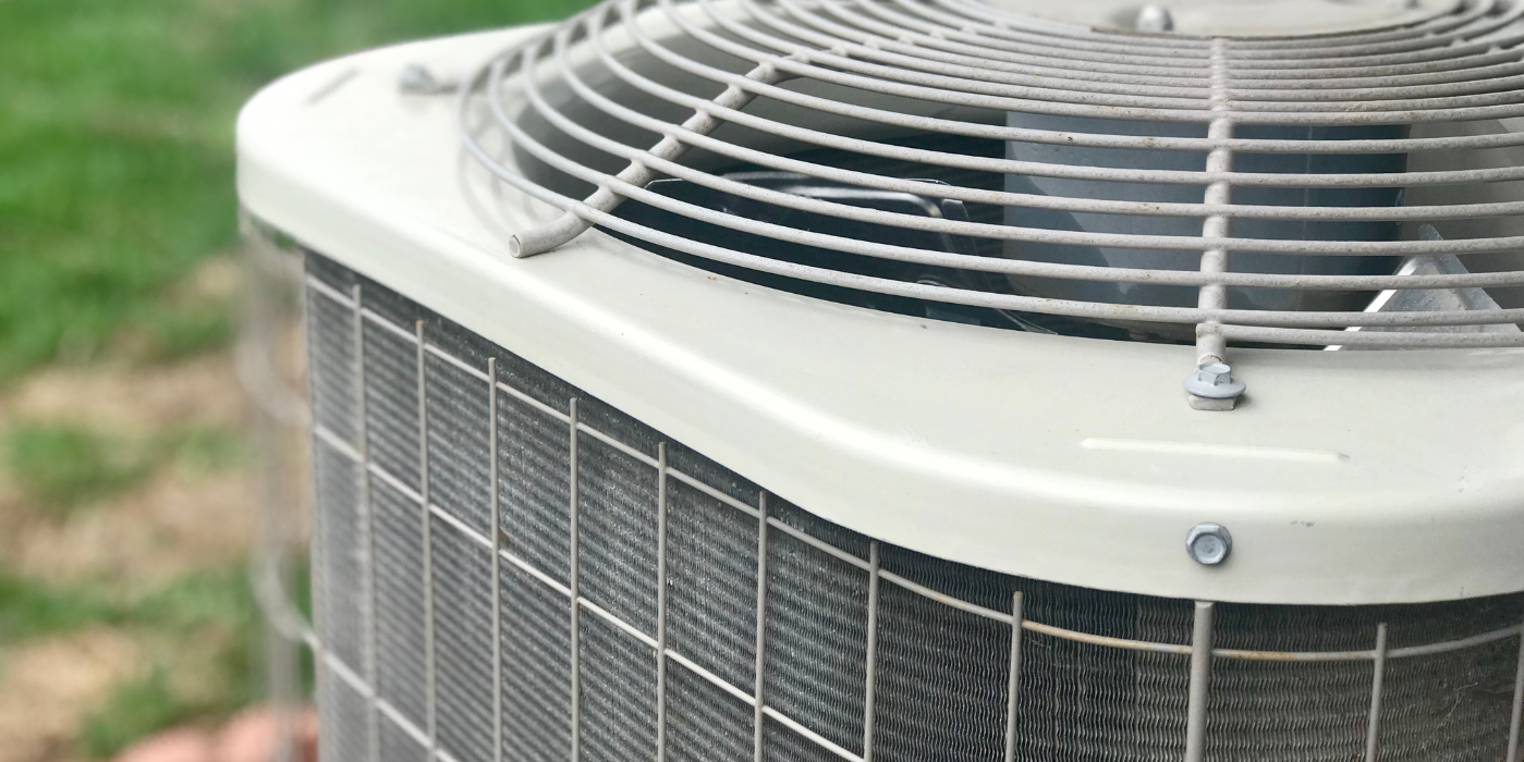 A person is holding an air conditioner outside in the grass.