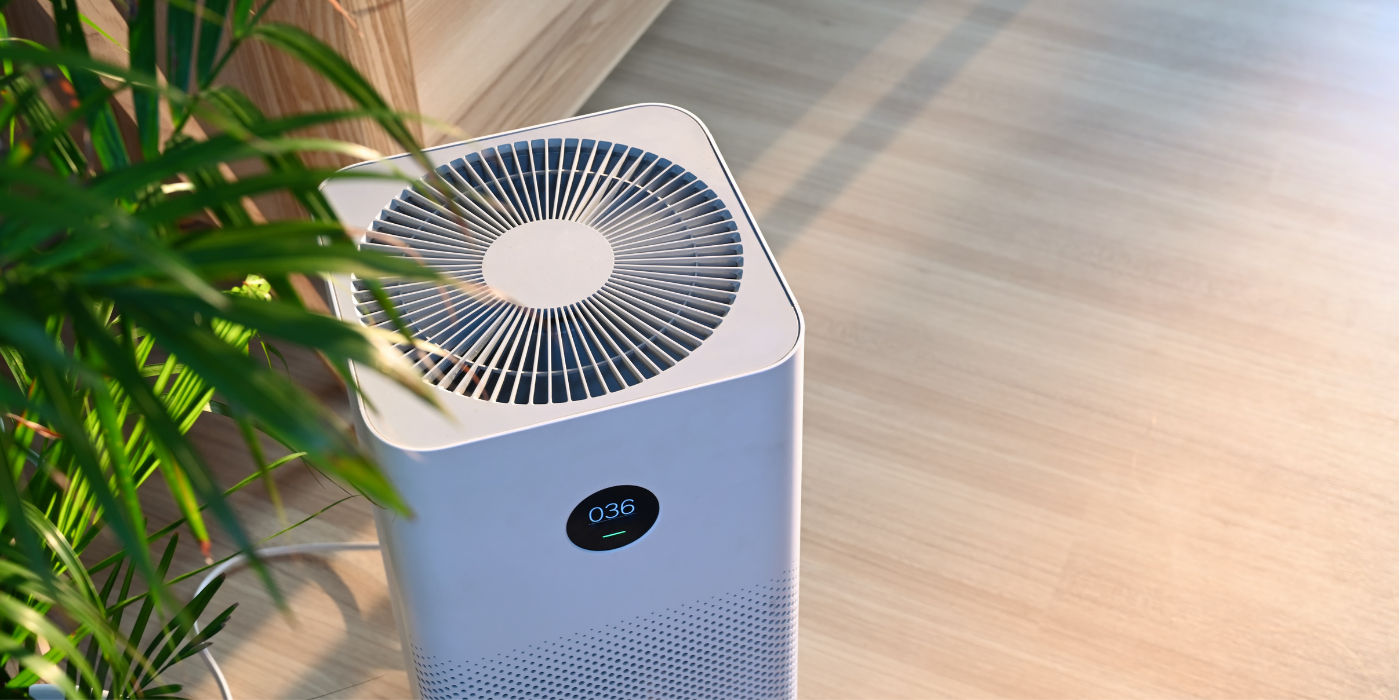 A white air purifier is sitting on a wooden floor next to a plant.