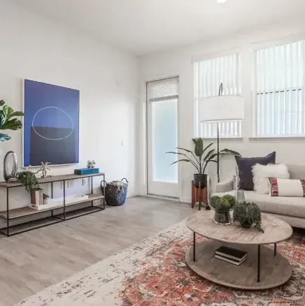 Bright minimalist living room with white sofa, round coffee table, blue wall art, and plants