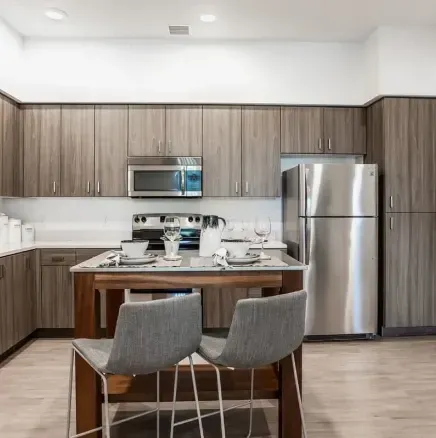 Modern kitchen with wood cabinets, stainless appliances, and a dining table set for two in the foreground
