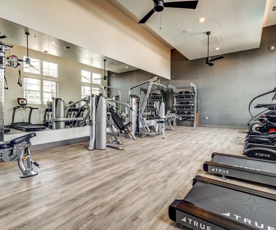 Bright gym interior with cardio machines, weight equipment, mirrors, and wood flooring