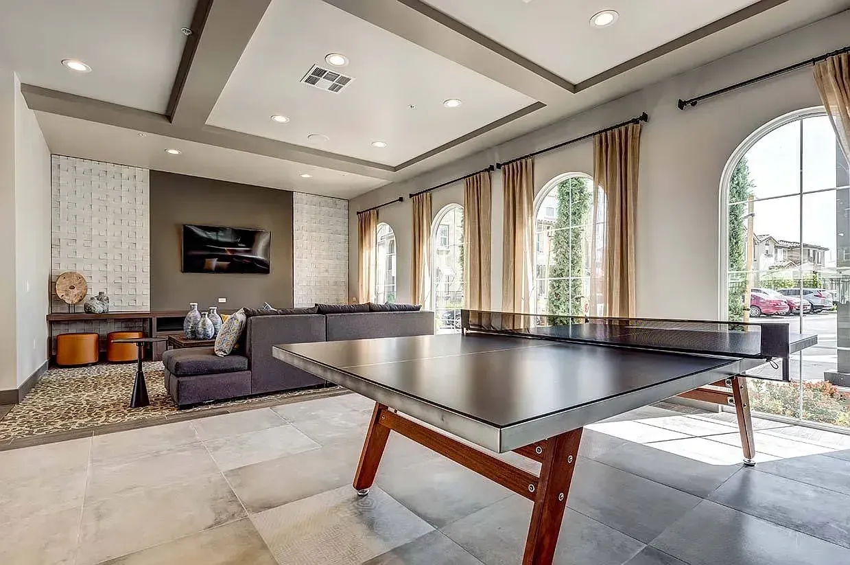 Modern living room with a ping-pong table, gray sofa, wall-mounted TV, and large arched windows