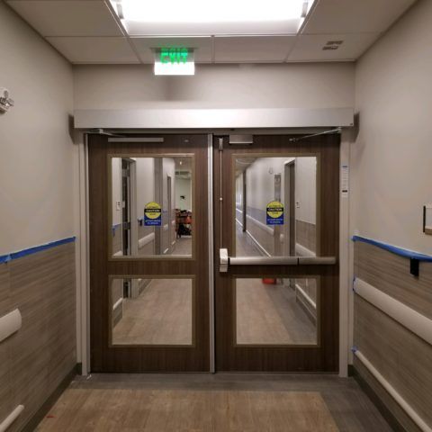 Automatic Doors Installation and Repair - A hospital hallway with a green exit sign above the doors
