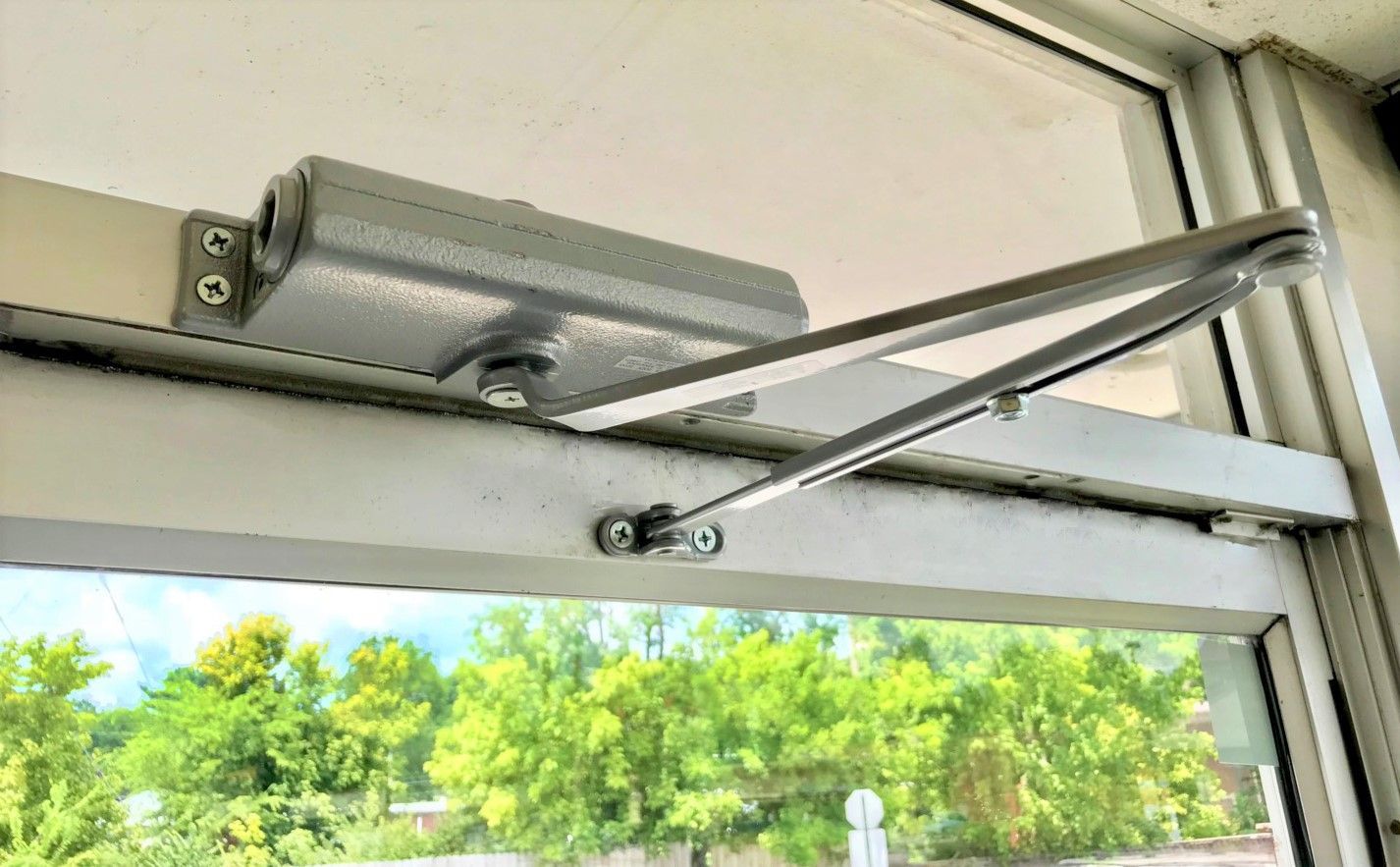 A close up of a door closer on a glass door.