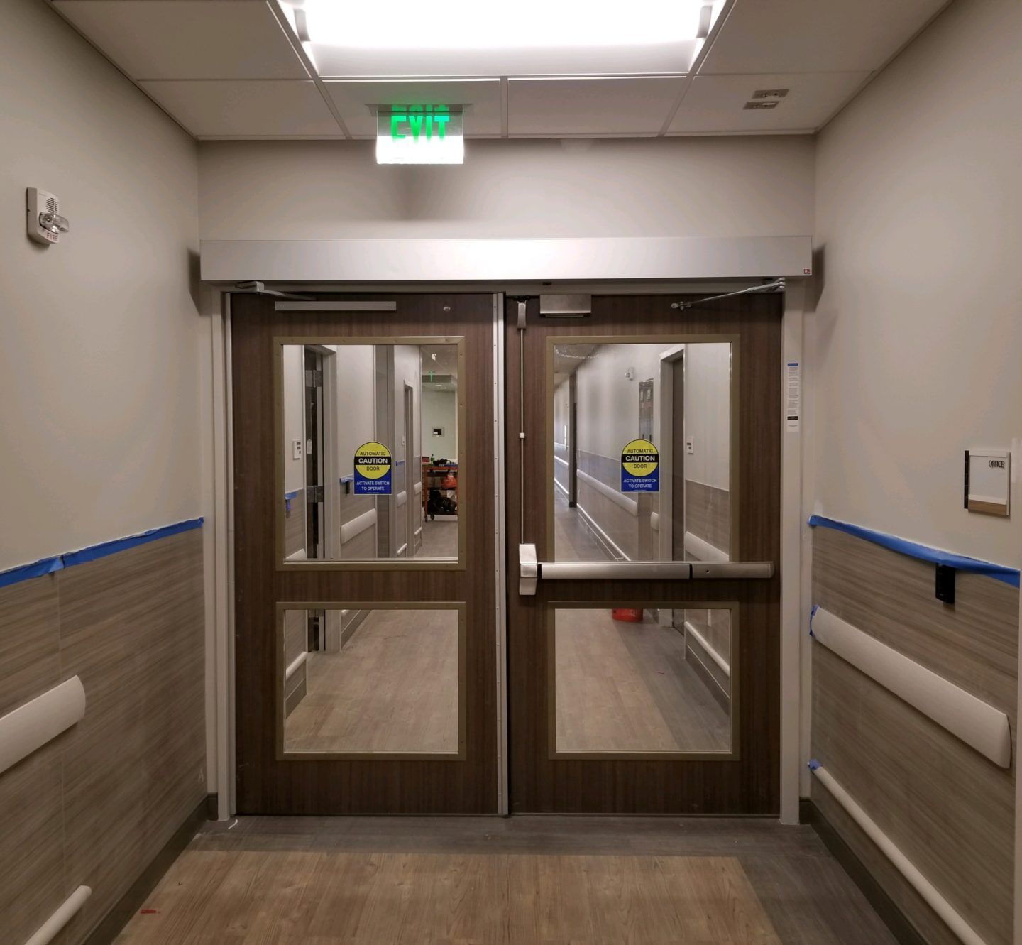 A hallway with a green exit sign above the doors
