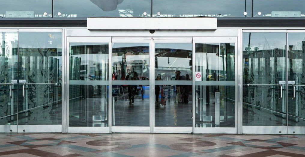 A large sliding glass door in a building with people walking through it.