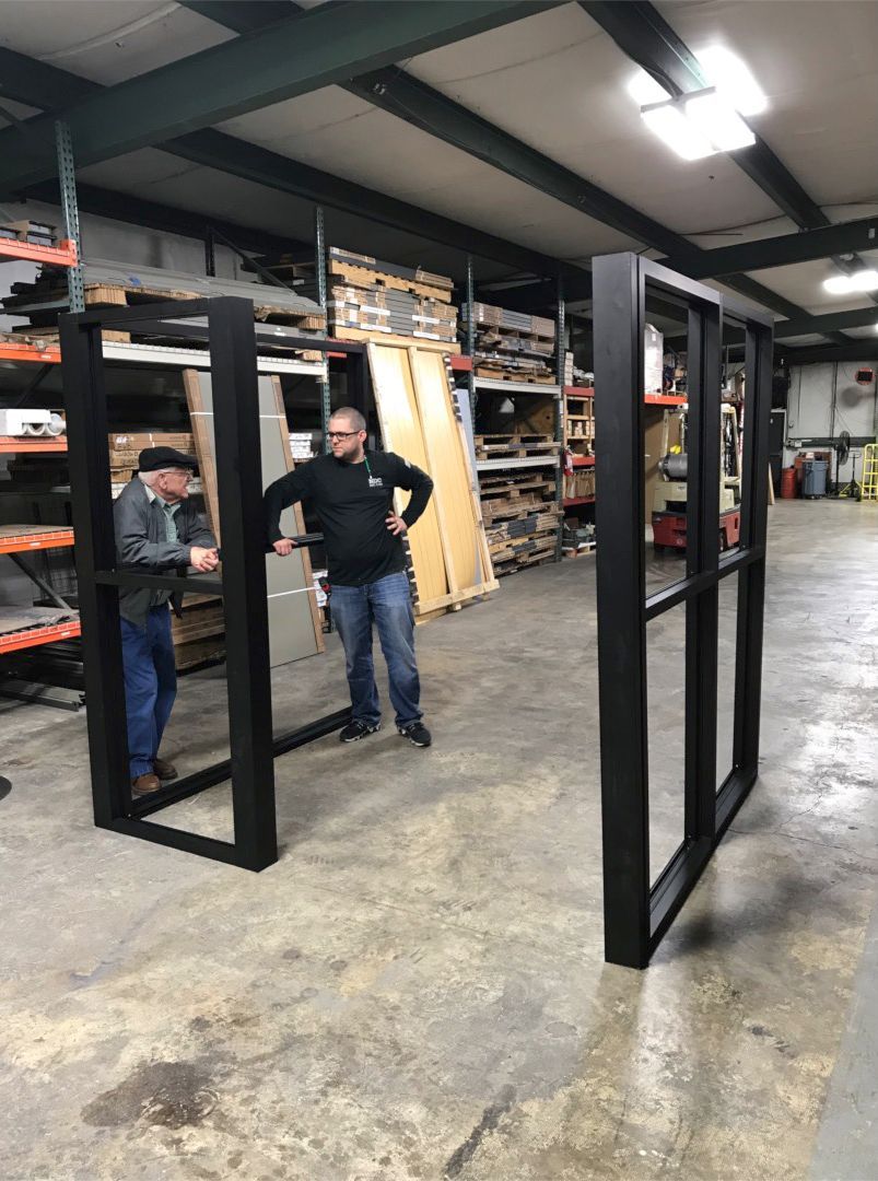 Storefronts & Glass Doors Installation and Repair - Two men are standing in a warehouse looking at a window frame.