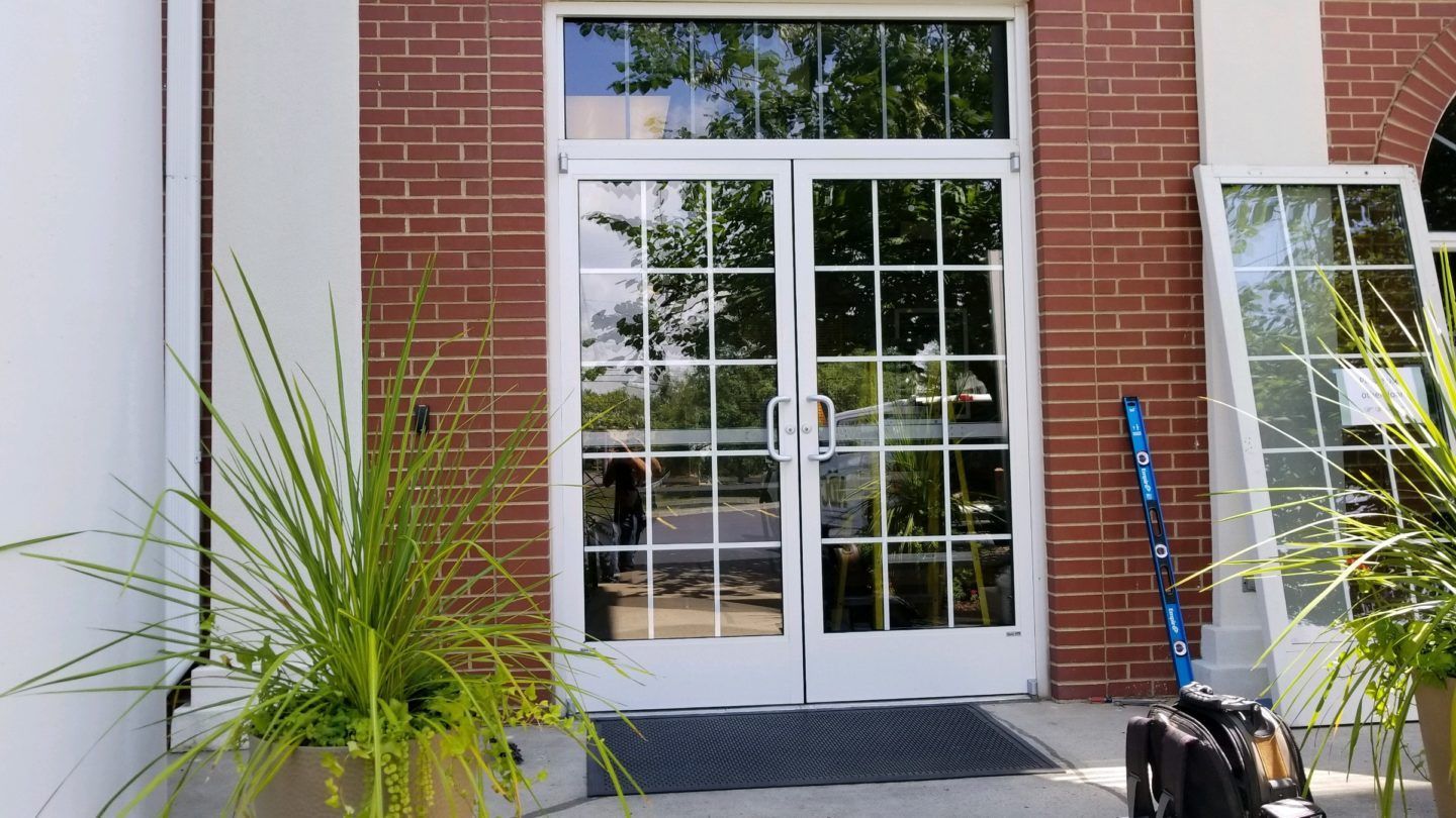 Storefronts & Glass Doors Installation and Repair - A brick building with a white door and a suitcase in front of it.