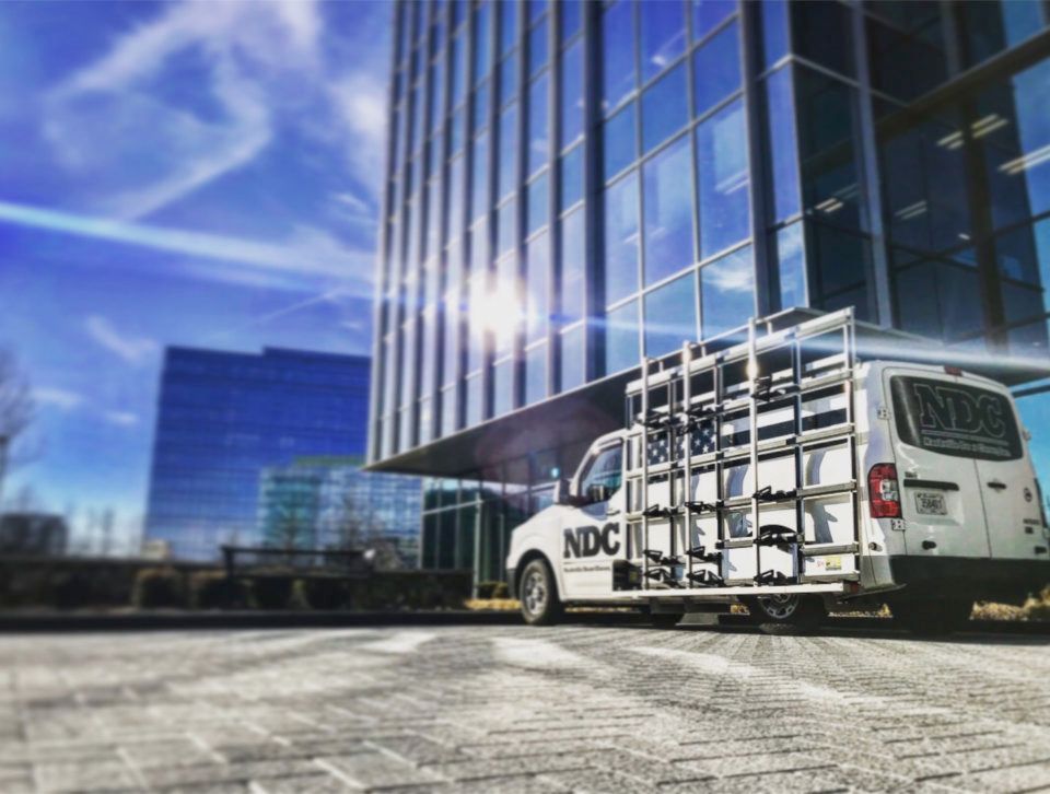 Storefronts & Glass Doors Installation and Repair - A white van is parked in front of a tall building.