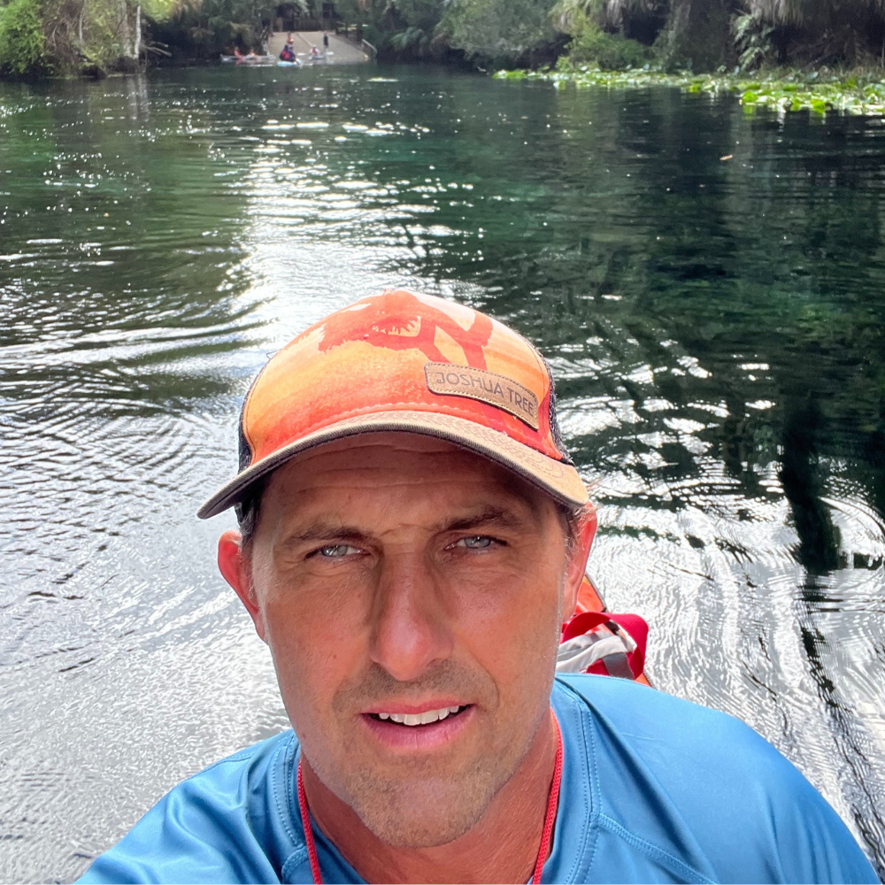 Man in orange cap on water, clear water and trees in the background.