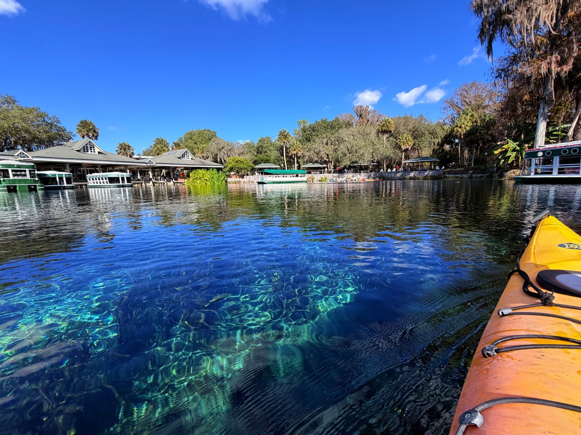 Kayak on clear, blue water; buildings and trees line the shore under a sunny sky.