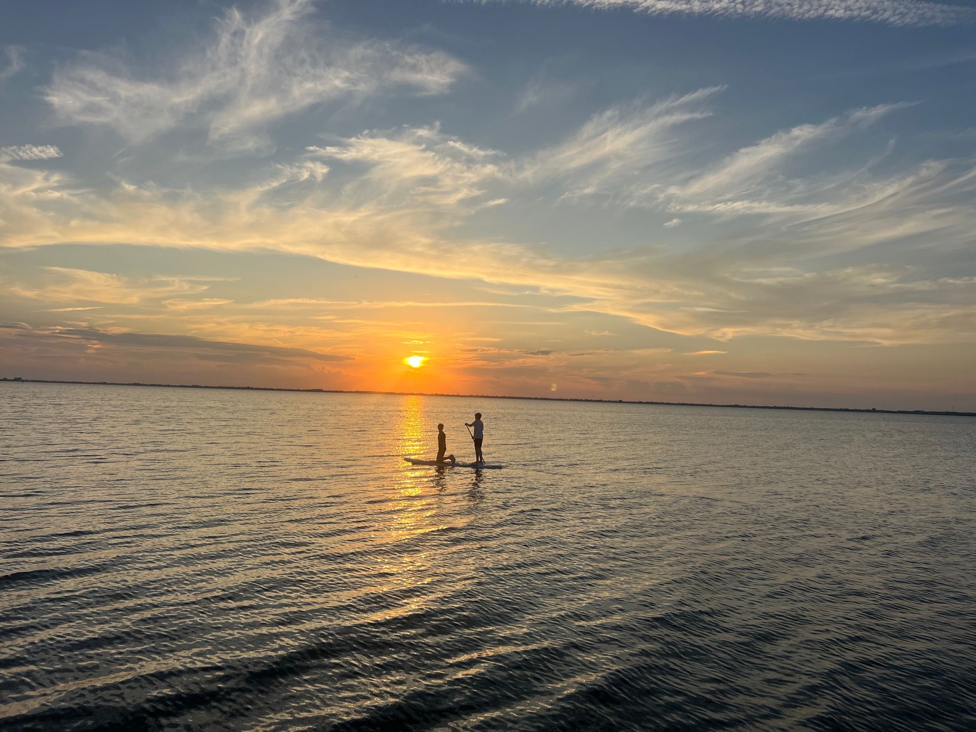 Two people paddleboarding at sunset on a calm body of water with orange and blue hues.