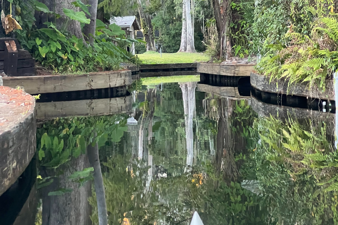 Water canal lined with concrete, reflecting trees and greenery.