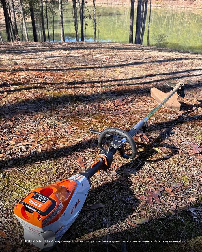 A stihl brush cutter is sitting on the ground in the woods.