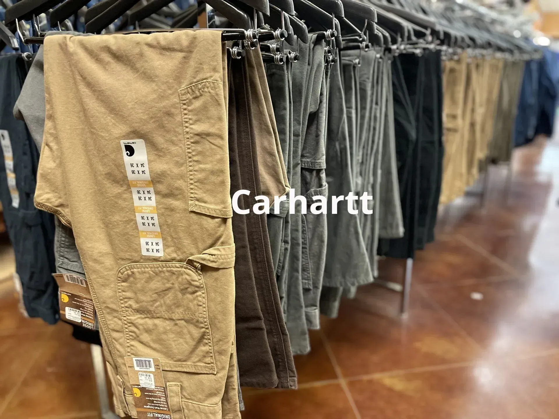 A row of carhartt pants hanging on a rack in a store.